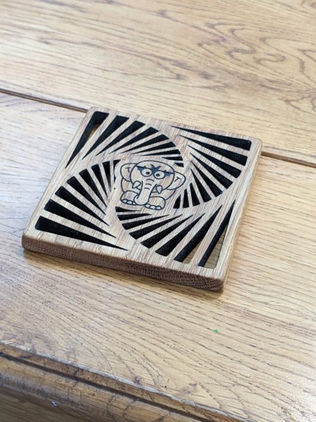 A wooden coaster featuring a swirl pattern and a central Bat-Ele design.