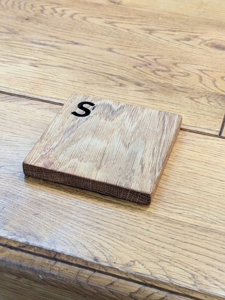 A wooden square coaster with an perosnalised name cut and engraved on the top left corner