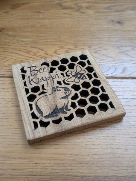 Wooden coaster with a bee, Cappiabarra and honeycomb design. Bee Kappi
